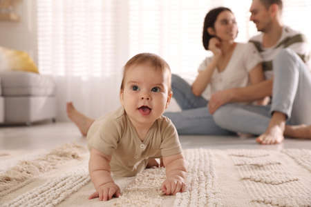 Happy parents watching their cute baby crawl on floor at homeの写真素材