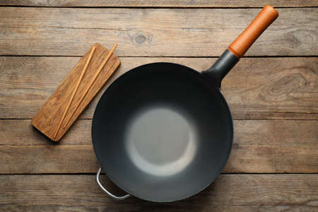 Empty iron wok with chopsticks on wooden table, flat layの写真素材