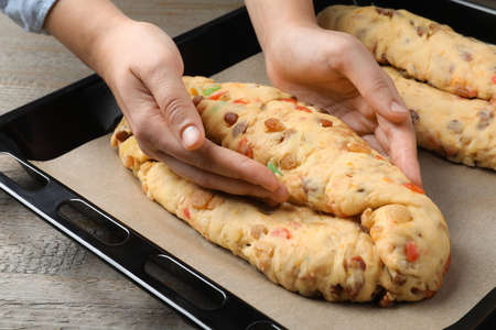 Woman making Stollen with candied fruits and nuts on baking tray at wooden table, closeup. Baking...