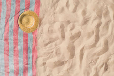 Towel with straw hat on sandy beach, top view. Space for text