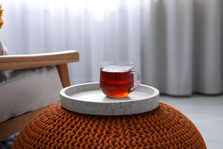 Tray with cup of tea on stylish knitted pouf in room. Interior designの写真素材