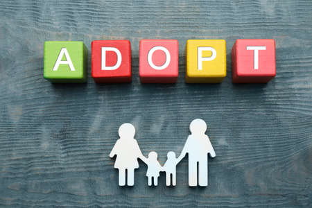 Family figure and word Adopt made of cubes on blue wooden table, flat layの写真素材