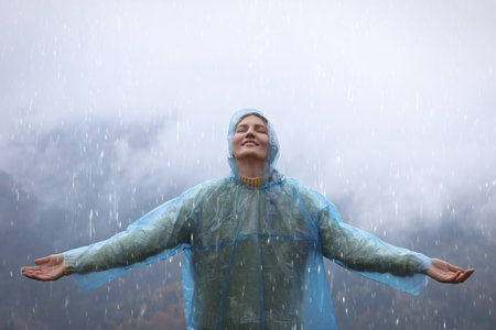 Young woman with raincoat enjoying rainy weather in mountainsの写真素材