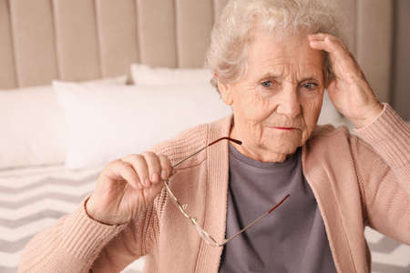 Senior woman with headache in bedroom at home