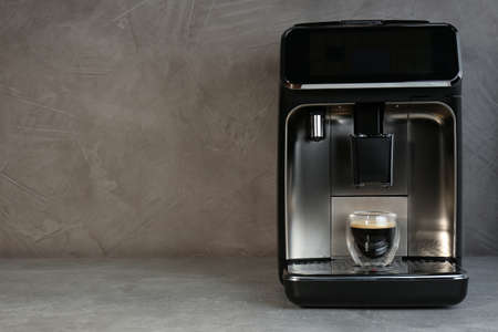 Modern espresso machine with glass of coffee on gray table, space for text