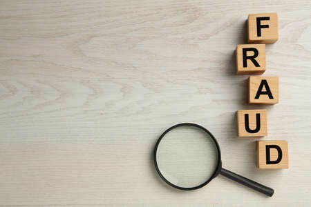 Wooden cubes with word Fraud and magnifying glass on white table, flat lay. Space for textの写真素材