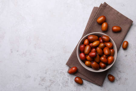 Fresh Ziziphus jujuba fruits with bowl and napkin on light table, flat lay. Space for textの写真素材