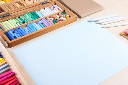 Blank paper, soft pastels and drawing pencils on wooden table at artist's workplace. Space for...