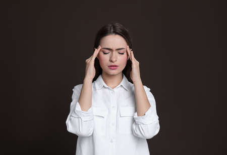 Young woman suffering from headache on brown background