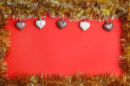 Frame of shiny golden tinsel and Christmas baubles on red background, flat lay. Space for text