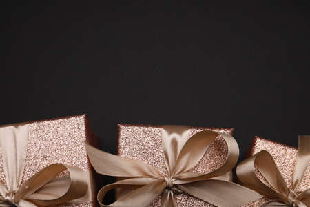 Shiny gift boxes with golden bows on black background, flat lay. Space for textの写真素材