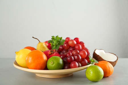 Wooden plate and different ripe fruits on gray table