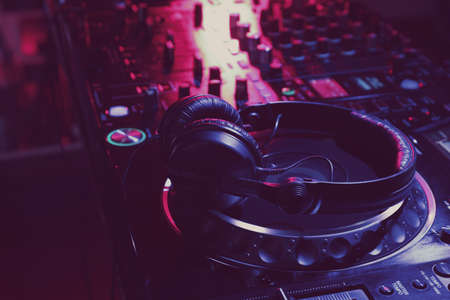 Closeup view of modern DJ controller with headphones on dark background