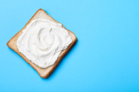 Slice of bread with tasty cream cheese on light blue background, top view. Space for textの写真素材