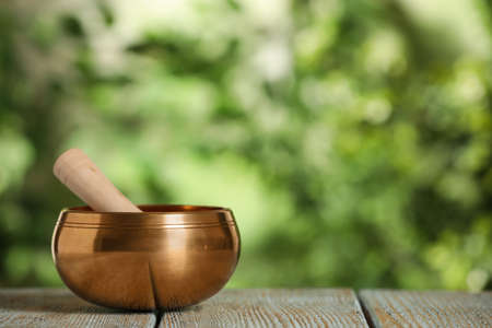 Golden singing bowl with mallet on wooden table outdoors, space for textの写真素材