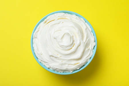 Bowl of tasty cream cheese on yellow background, top viewの写真素材