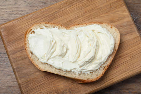 Slice of bread with tasty cream cheese on wooden table, top viewの写真素材