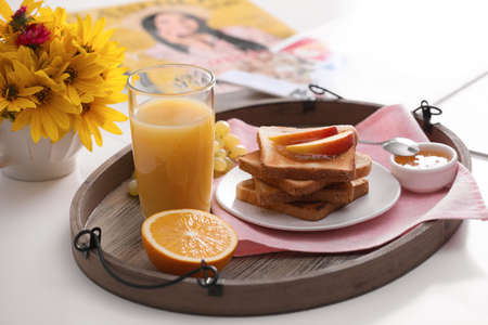 Wooden tray with delicious breakfast and beautiful flowers on white table