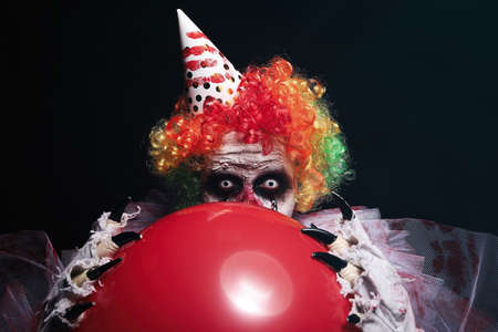 Terrifying clown with red air balloon on black background. Halloween party costumeの写真素材