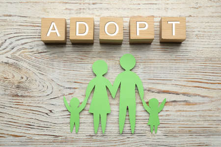 Family figure and word Adopt made of cubes on white wooden table, flat lay