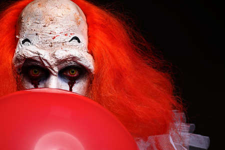 Terrifying clown with red air balloon on black background. Halloween party costumeの写真素材