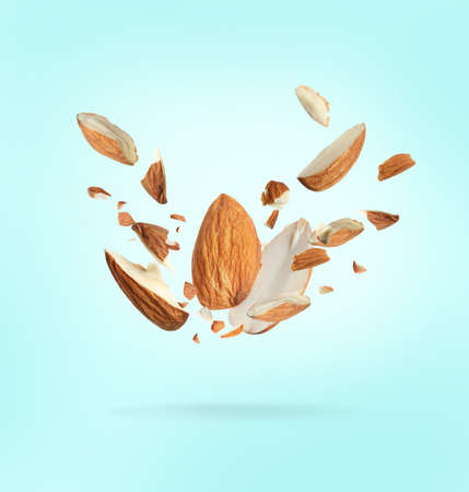 Pieces of tasty almonds falling on light blue background