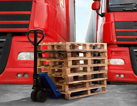Modern manual forklift with wooden pallets near trucks outdoorsの写真素材