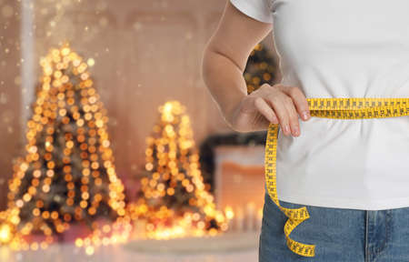 Woman measuring waist with tape in room decorated for Christmas, closeupの写真素材