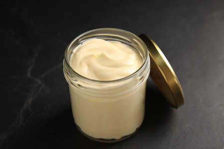 Jar of delicious mayonnaise and lid on black tableの写真素材