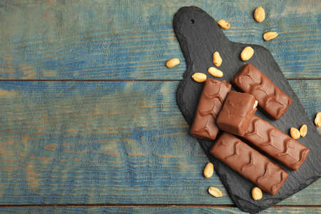 Slate board of chocolate bars with nuts on light blue wooden table, top view. Space for textの写真素材