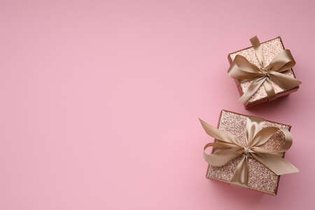 Shiny gift boxes with golden bows on pink background, flat lay. Space for textの写真素材