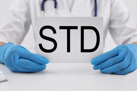 Doctor holding sheet of paper with abbreviation STD at white table, closeupの写真素材