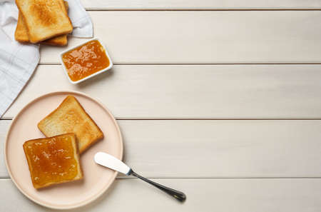 Toasts and orange jam served on white wooden table, flat lay. Space for textの写真素材