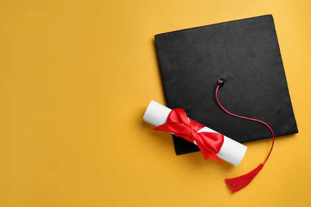 Graduation hat and diploma on yellow background, flat lay. Space for textの写真素材