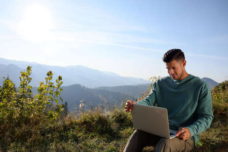 Man working on laptop outdoors surrounded by beautiful natureの写真素材