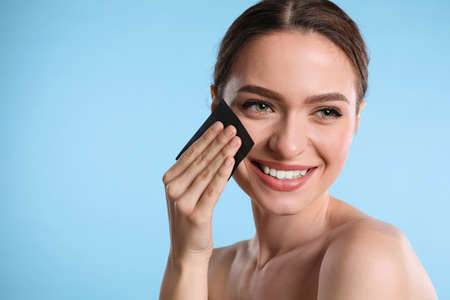 Beautiful woman using mattifying wipe on light blue background, space for textの写真素材