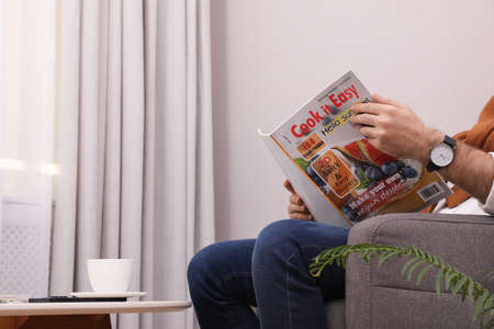 Man reading magazine in armchair at home, closeup