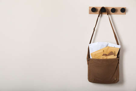 Brown postman bag with newspapers and mails hanging on light wall, space for text