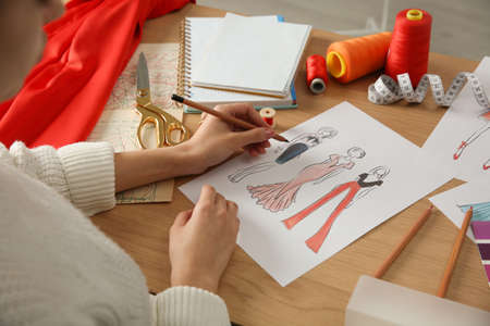 Fashion designer creating new clothes in sketchbook at wooden table, closeup