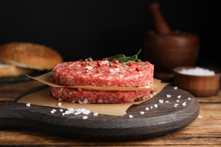 Raw hamburger patties with rosemary and spices on wooden table, closeupの写真素材