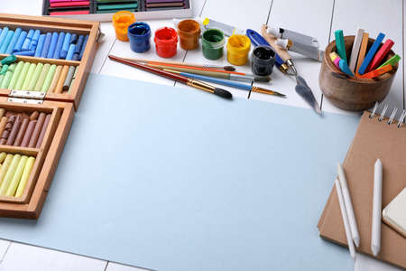 Blank sheet of paper, colorful chalk pastels and other drawing tools on white wooden table. Modern artist's workplaceの写真素材