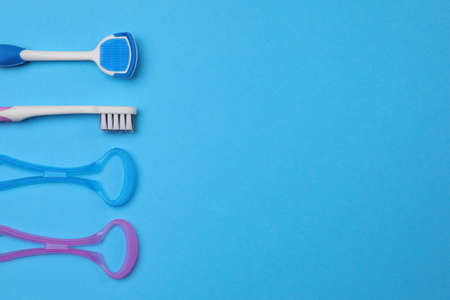 Tongue cleaners and toothbrush on blue background, flat lay. Space for text