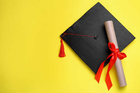 Graduation hat and diploma on yellow background, flat lay. Space for textの写真素材