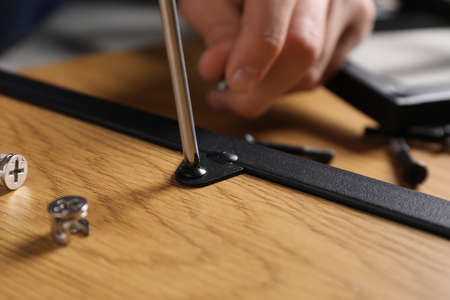 Man with screwdriver assembling wooden furniture indoors, closeup