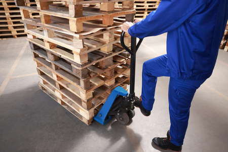 Worker moving wooden pallets with manual forklift in warehouse, closeup