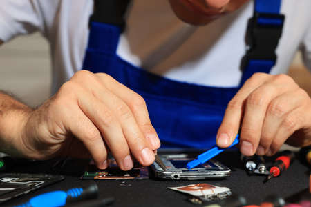 Technician repairing broken smartphone at table, closeup