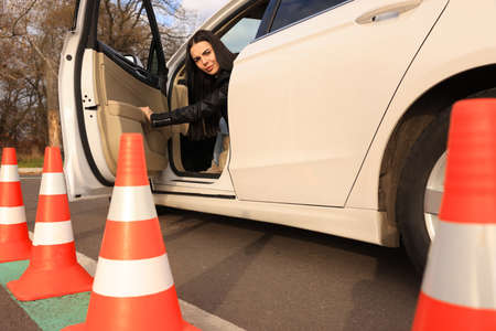 Young woman in car on test track with traffic cones, low angle view. Driving school