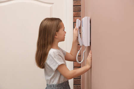 Cute little girl answering intercom call indoors