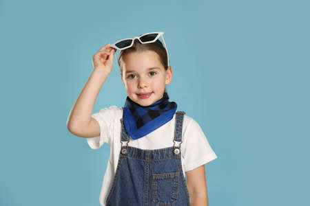 Cute little girl wearing stylish bandana and sunglasses on turquoise backgroundの写真素材