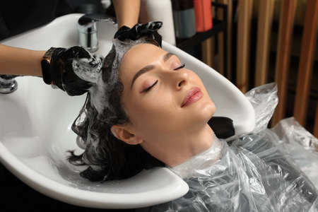 Hairdresser rinsing out dye from woman's hair in beauty salon